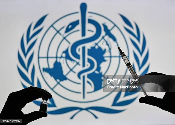 An illustrative image of a person holding a medical syringe and a Covid-19 vaccine vial in front of the World Health Organization logo displayed on a...