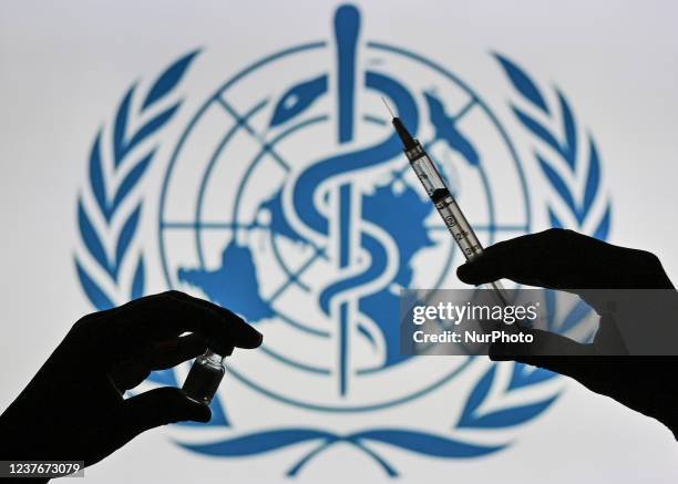 An illustrative image of a person holding a medical syringe and a Covid-19 vaccine vial in front of the World Health Organization logo displayed on a...