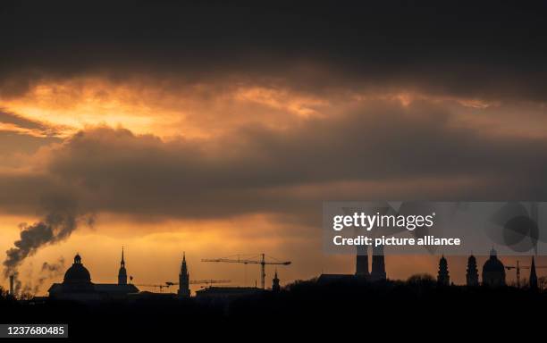 January 2022, Bavaria, Munich: The skyline of downtown Munich can be seen in the brilliant light of the sunset. In the background the dome of the...