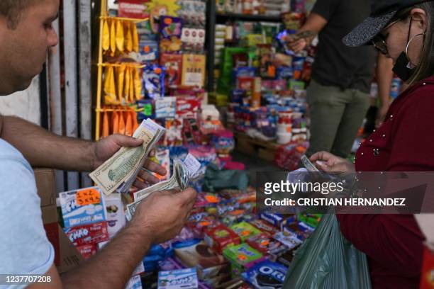 Grocery vendor counts Venezuelan bolivares and US dollar notes with a costumer, in Caracas, on January 13, 2022. - Despite the fact that the country...