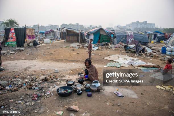 Slum dweller woman seen washing utensils in an unhygienic space in front of slum clusters. Poor people living in urban slum area of vasundhara, Urban...