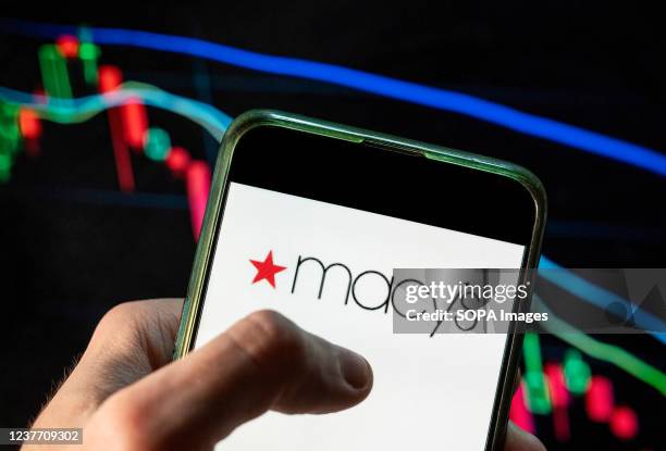 In this photo illustration the American department store chain Macy's logo seen displayed on a smartphone with an economic stock exchange index graph...