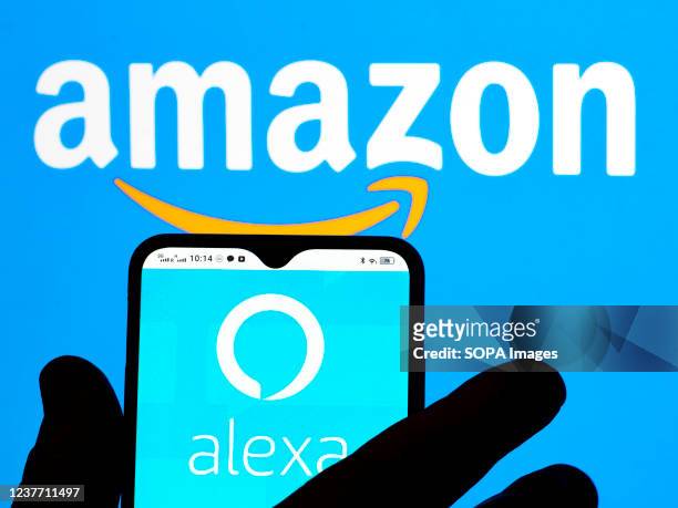 In this photo illustration, the Amazon Alexa logo is seen displayed on a smartphone screen and Amazon logo in the background.