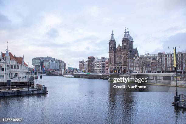 The canals and parked boats in Amstedam with the Basilica of Saint Nichola and NEMO Science museum in the backround. Locals and a few tourists at the...