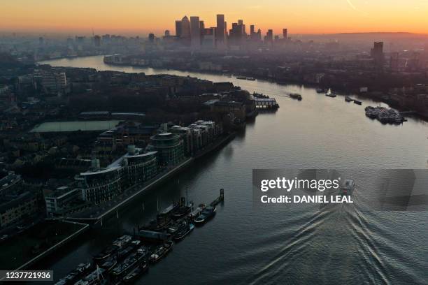 An overhead view shows a boat passing the Hermitage Community Moorings on The River Thames as the sun rises behind the office buildings of the Canary...