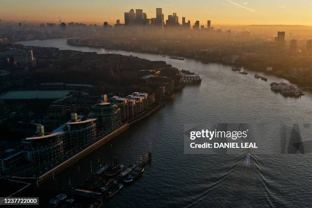 An overhead view shows a boat passing the Hermitage Community Moorings on The River Thames as the sun rises behind the office buildings of the Canary...