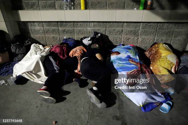 Migrants sleep on a sidewalk as they wait to form a caravan aiming to reach the United States on January 15, 2022 in San Pedro Sula, Honduras....