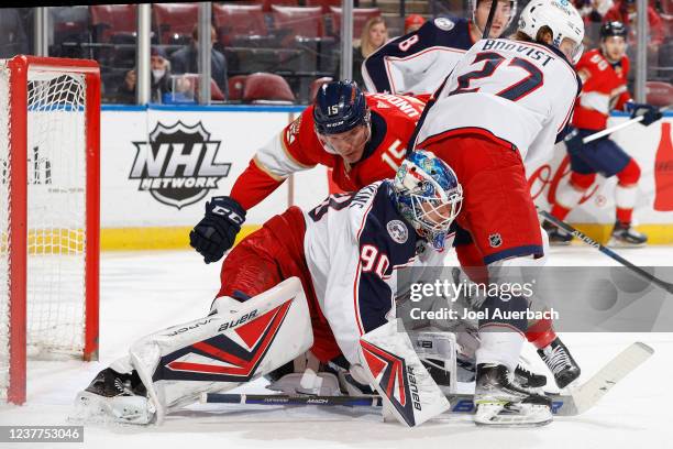 Goaltender Elvis Merzlikins of the Columbus Blue Jackets covers the puck as Anton Lundell of the Florida Panthers looks for a rebound during first...