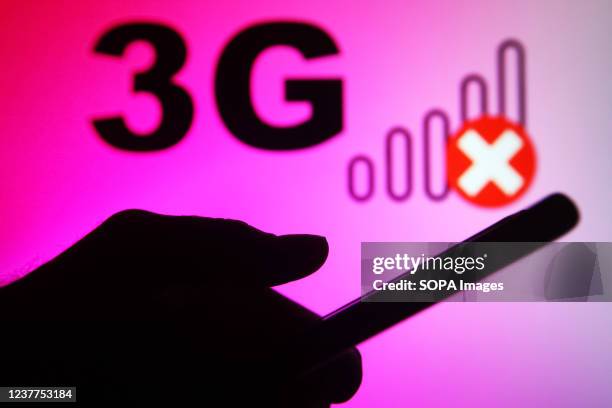 In this photo illustration, a 3G sign and no signal icon are seen in the background, and a silhouette of a hand holding a smartphone in front of it.