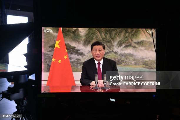 Chinese President Xi Jinping is seen on a TV screen speaking remotely at the opening of the WEF Davos Agenda virtual sessions at the WEF's...