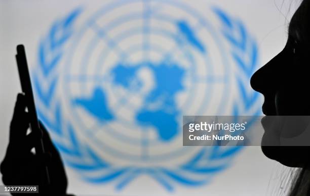 An image of a woman holding a cell phone in front of the UN logo displayed on a computer screen. On Tuesday, January 12 in Edmonton, Alberta, Canada.