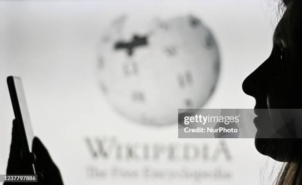 An image of a woman holding a cell phone in front of the Wikipedia logo displayed on a computer screen. On Tuesday, January 12 in Edmonton, Alberta,...
