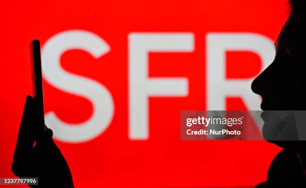 An image of a woman holding a cell phone in front of the SFR logo displayed on a computer screen. On Tuesday, January 12 in Edmonton, Alberta, Canada.