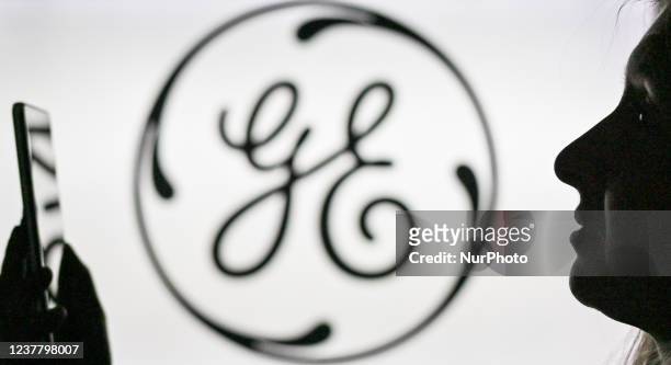 An image of a woman holding a cell phone in front of the GE logo displayed on a computer screen. On Tuesday, January 12 in Edmonton, Alberta, Canada.