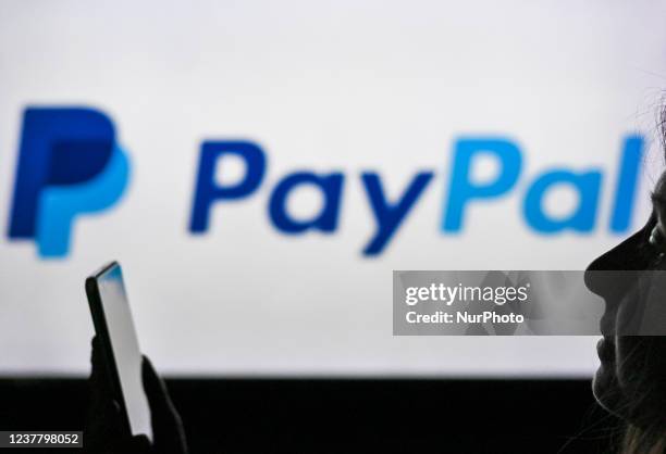 An image of a woman holding a cell phone in front of the PayPal logo displayed on a computer screen. On Tuesday, January 12 in Edmonton, Alberta,...