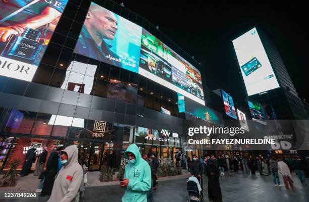 People walk beneath advertisement billboards at Boulevard entertainment city in the Saudi capital Riyadh, late on January 19, 2022.