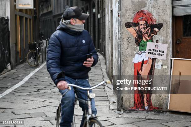 Man cycles past a mural entitled "Thank goodness Silvia is here" , representing former Italian prime minister and presidential candidate Silvio...