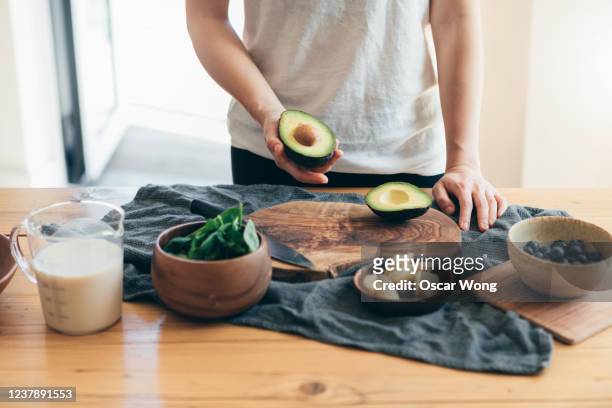 young woman making healthy smoothie for breakfast - cutting avocado stockfoto's en -beelden