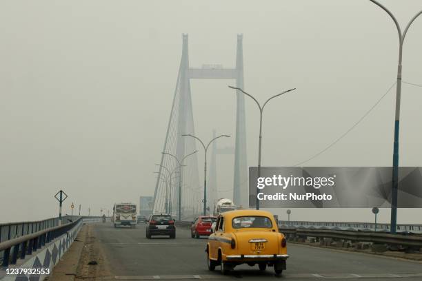 Yellow Ambassador taxi cross the Vidyasagar Bridge over the Ganga River amid smoggy conditions on January 23, 2022 in Kolkata, West Bengal, India.