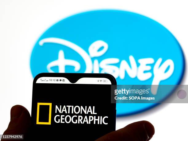 In this photo illustration, the National Geographic logo is seen displayed on a smartphone screen with a Disney logo in the background.