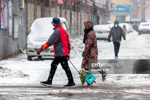 This photo taken on January 23, 2022 shows people walking on a street during snowfall as the city starts to reopen after a Covid-19 coronavirus...