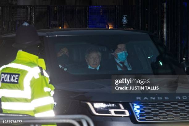 Police officer watches as Britain's Prime Minister Boris Johnson , wearing a face covering to help mitigate the spread of Covid-19 but pulled down...