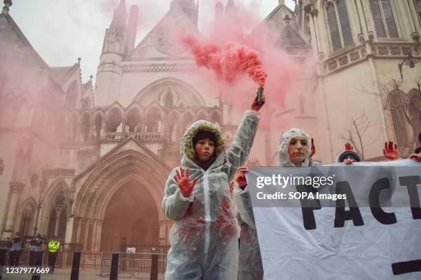 An activist wearing a hazmat suit splashed in fake blood holds a smoke flare during the protest. Animal rights activists gathered outside the Royal...