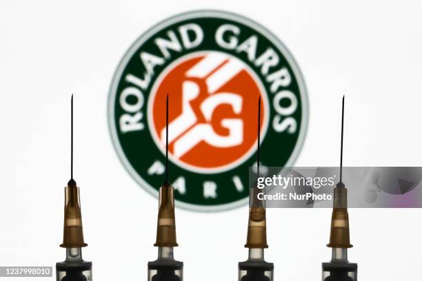 Medical syringes and Roland Garros logo displayed on a screen in the background are seen in this illustration photo taken in Krakow, Poland on...