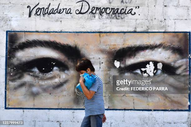 Woman walks past a mural portraying the eyes of late Venezuelan president Hugo Chavez that reads "True Democracy", in downtown Caracas on January 26,...