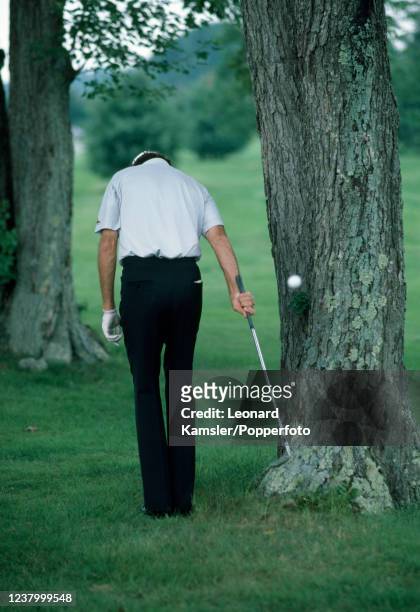 American professional golfer Dale Douglas hitting backwards one-handed out of a difficult lie adjacent to a tree, circa 1986.