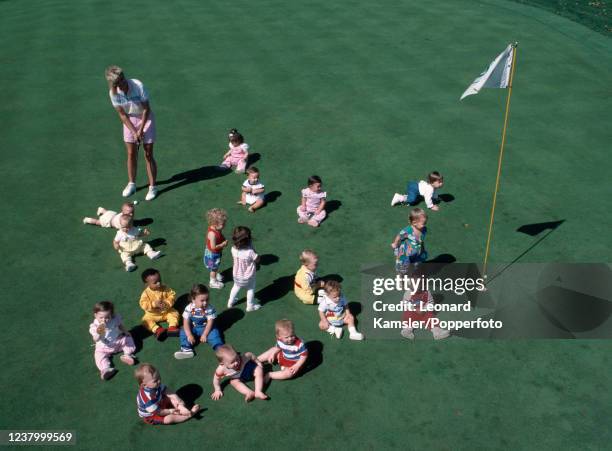 An overhead shot of the youngest of potential golfers being introduced to the game by a lady golfer putting through a group of them seated and...