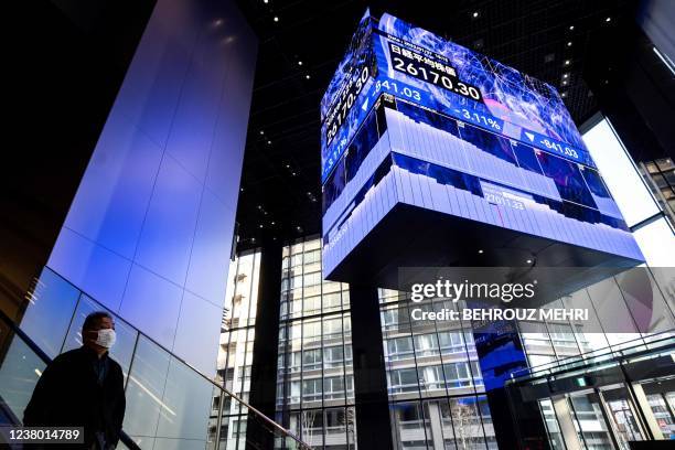 Person rides down an escalator next to an electronic quotation board displaying closing numbers of the Nikkei 225 index of the Tokyo Stock Exchange...