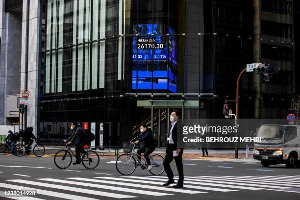 People cross a road near an electronic quotation board displaying closing numbers of the Nikkei 225 index of the Tokyo Stock Exchange in Tokyo on...