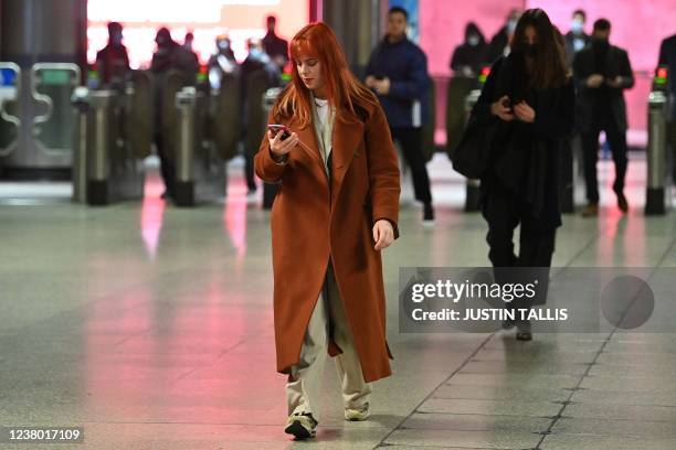 Commuters, with and without face coverings, walk out of a tube station in central London on January 27, 2022. - Commuters in England went back to...