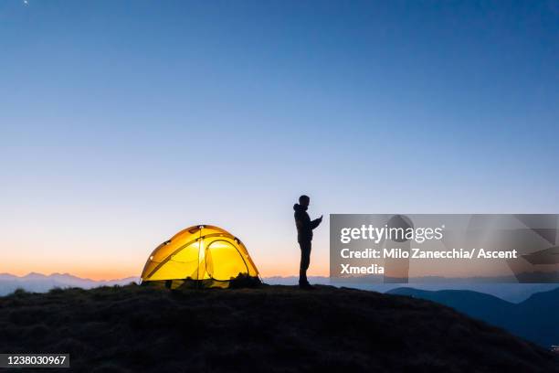 distant view of a man using his cell phone outside of his tent at twilight - ict mobiles stock-fotos und bilder