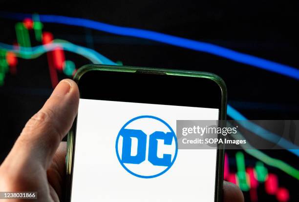 In this photo illustration the American comic book publisher company DC Comics logo seen displayed on a smartphone with an economic stock exchange...