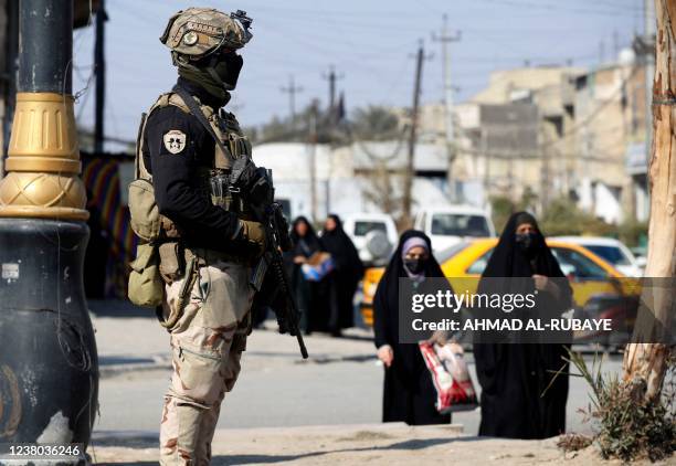 Women walk past Iraqi soldiers manning a checkpoint in the capital Baghdad on January 28 following a reported rocket attack on the country's airport....