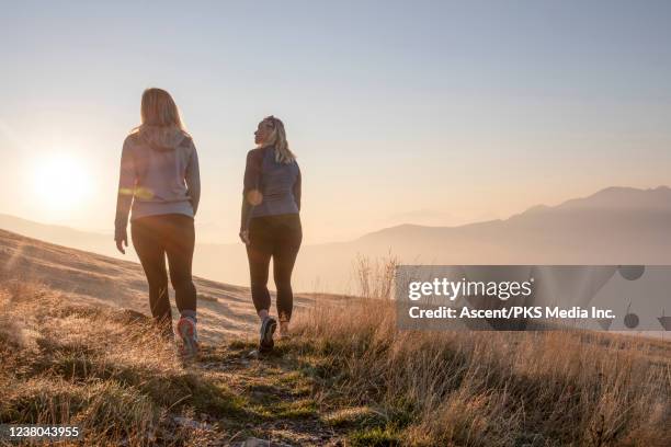 two women walk along an alpine path at sunrise - long hair back stock pictures, royalty-free photos & images