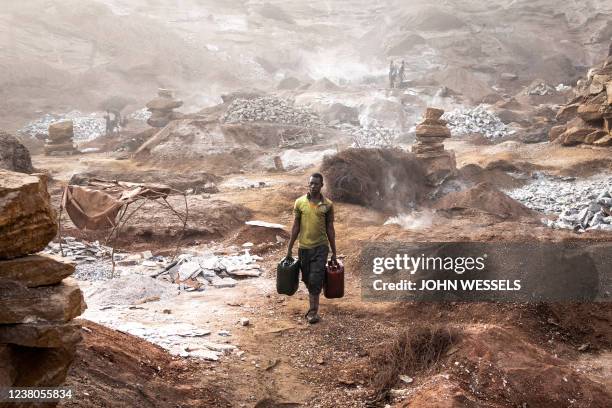 Man carries drums of water through Pissy Granite Mine in the centre of Ouagadougou on January 29, 2022. Surrounded by roads, houses and...