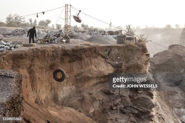 Man throws a tyre off the edge of Pissy Granite Mine in the centre of Ouagadougou on January 29, 2022. He will burn the tyre on the granite to help...