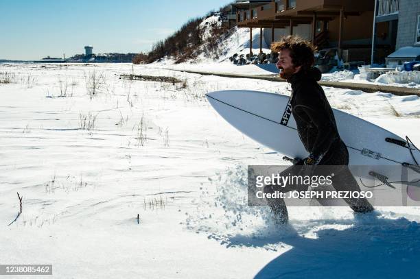 Surfer makes his way through deep snow to the ocean in Winthrop, Massachusetts, on January 30, 2022. - Surfers looked to catch the waves caused by...