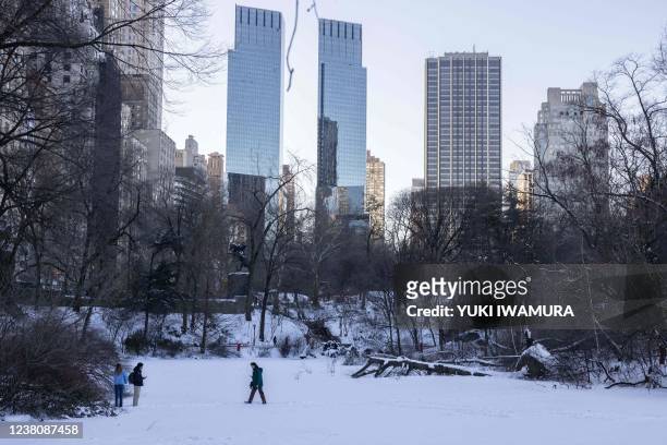 People walk on a frozen lake in Central Park in New York City on January 30, 2022. - Blinding snow whipped up by powerful winds pummeled the eastern...