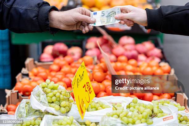 January 2022, Lower Saxony, Hanover: A customer pays for his purchase at a stall at a weekly market with a five-euro bill . After the price surge in...