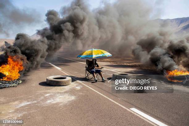 Demonstrator sits under an umbrella while blocking an access route to Iquique, Chile, during a regional strike called by different organizations...