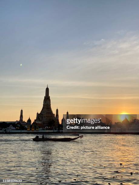 January 2022, Thailand, Bangkok: Wat Arun, the Temple of Dawn, seen at dusk from across the Chao Phraya River. Most tourist attractions are still...