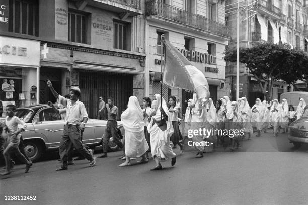 Algerian people, including veiled women, waving National Liberation Front and now independent Algerian state flags, head towards the Prefecture of...