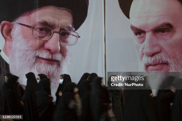 Iranian veiled women stand in front of portraits of Irans Supreme Leader Ayatollah Ali Khamenei and Late Leader Ayatollah Ruhollah Khomeini while...