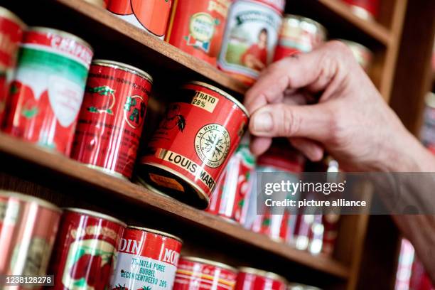 February 2022, Lower Saxony, Oldenburg: Gunda Tuchenhagen takes one of numerous tomato paste cans from different countries from a shelf in her dining...