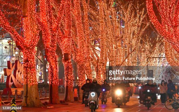 People on e-bikes pass a street with festive lights on the trees in Handan in north Chinas Hebei province Sunday, Jan. 30, 2022.