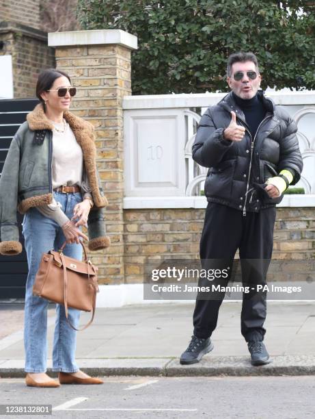 Simon Cowell shows the broken arm he suffered in a bicycle injury last week as he and his partner, Lauren Silverman, leave their home in London's...